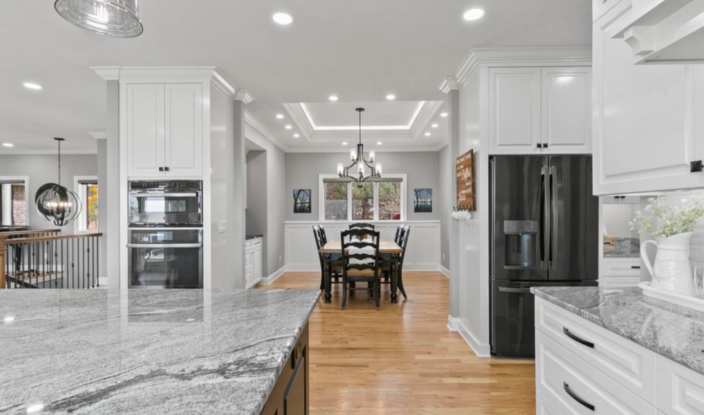 A modern, white kitchen with hardwood floors and recessed ceiling lights